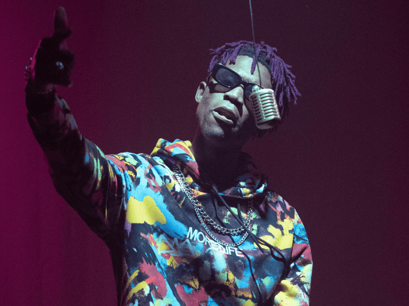 A person with purple hair wearing a tie dye hoodie and a microphone